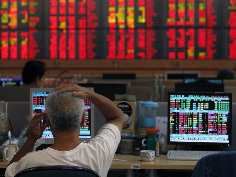 Un operador de Wall Street con pantallas en rojo de fondo, acciones